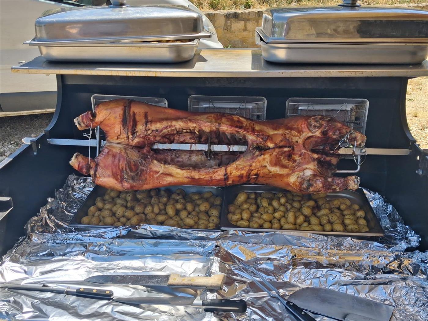 Cochon entier cuit à la broche au-dessus des pommes de terre, traiteur dans le Gard